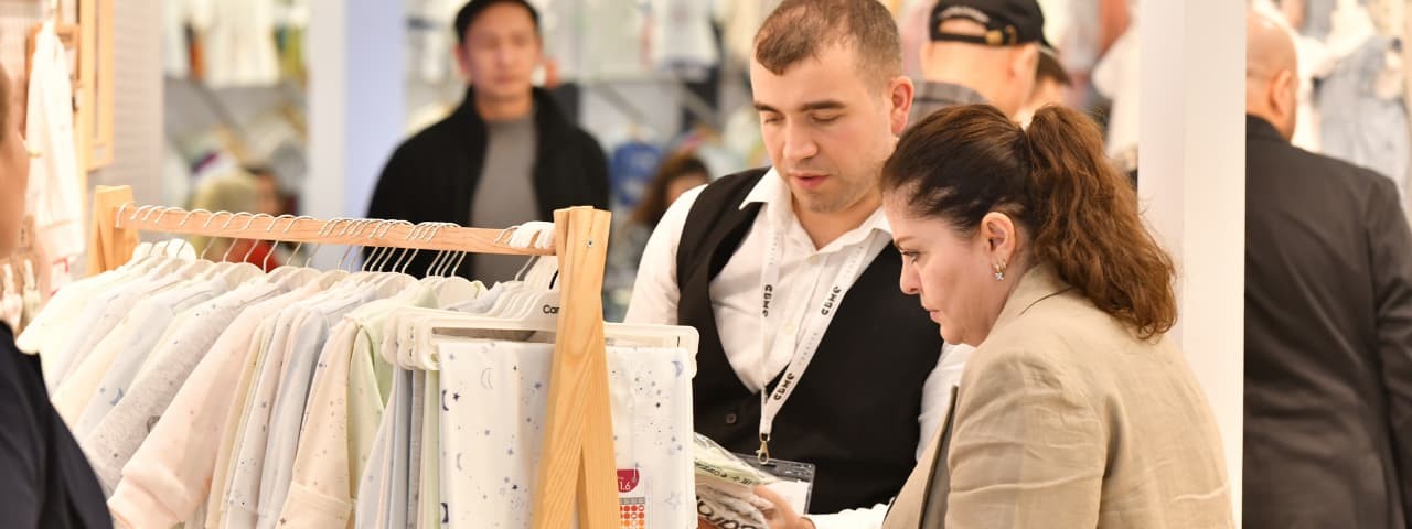 Two attendees at the CMBE Turkey exhibition closely examining the displayed clothing items.