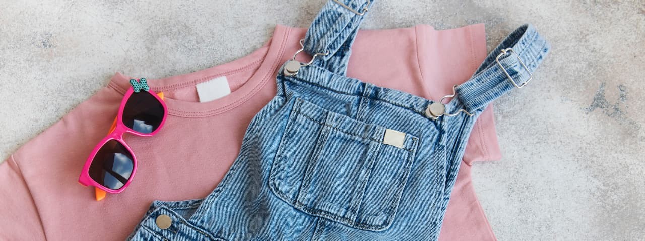 Children's clothing: a denim overalls, a pink sweatshirt, and pink sunglasses.