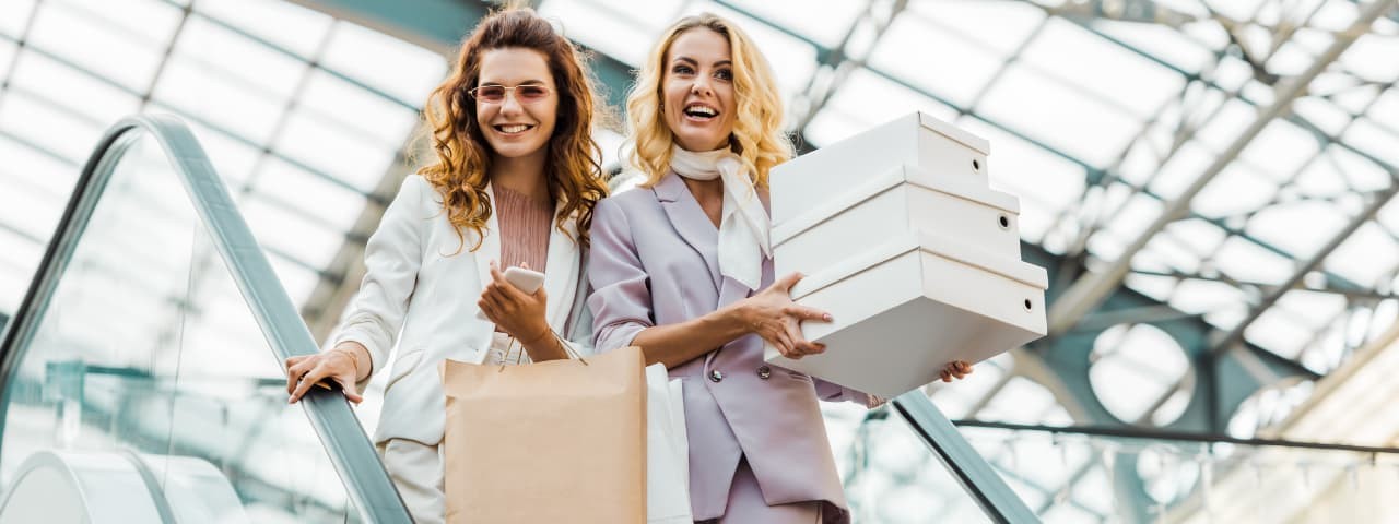 Yürüyen merdivende alışveriş çantaları ve kutular taşıyan iki kız.